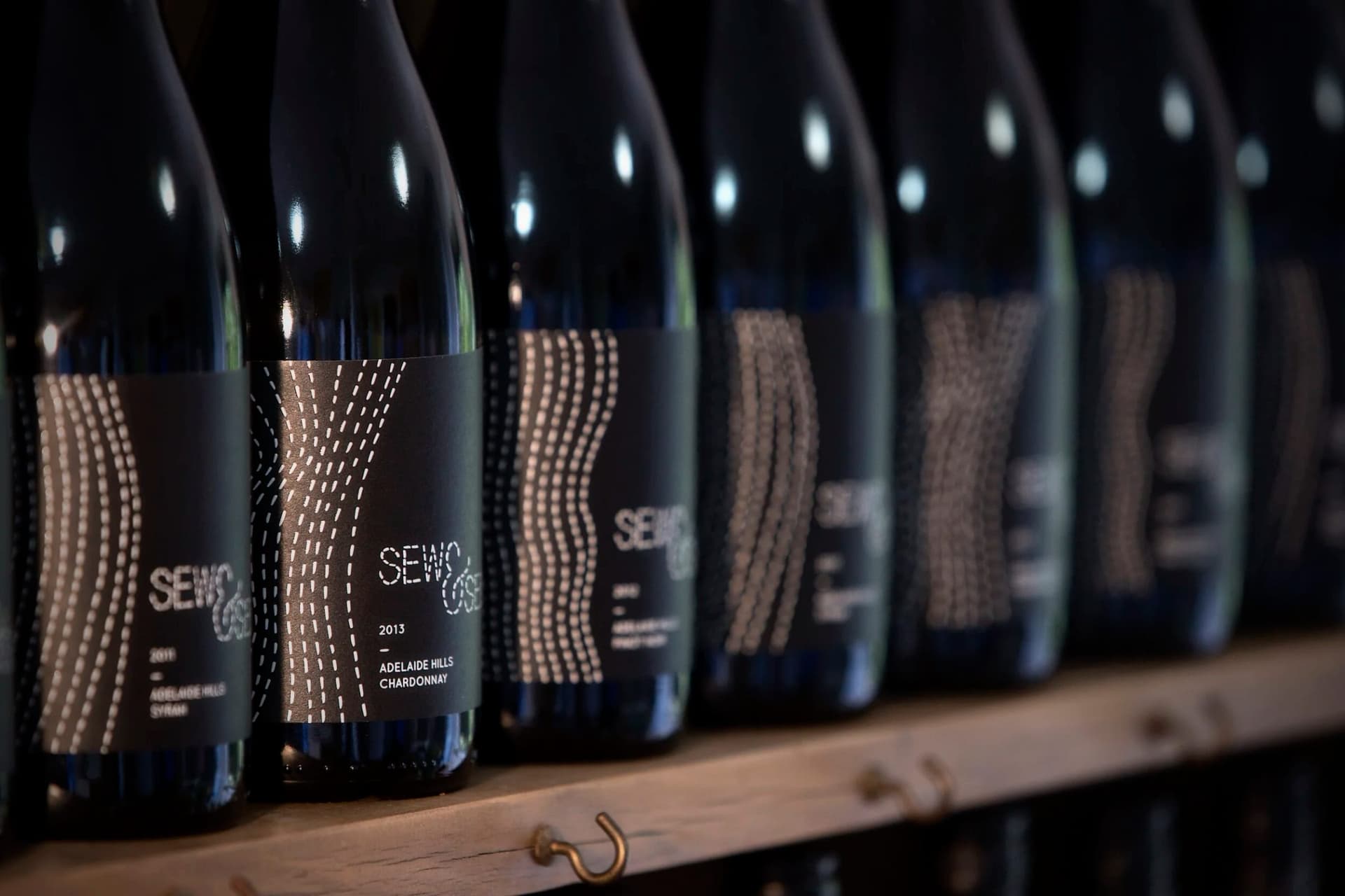 A shelf of Sew & Sew bottles with stitched labels in low cellar light