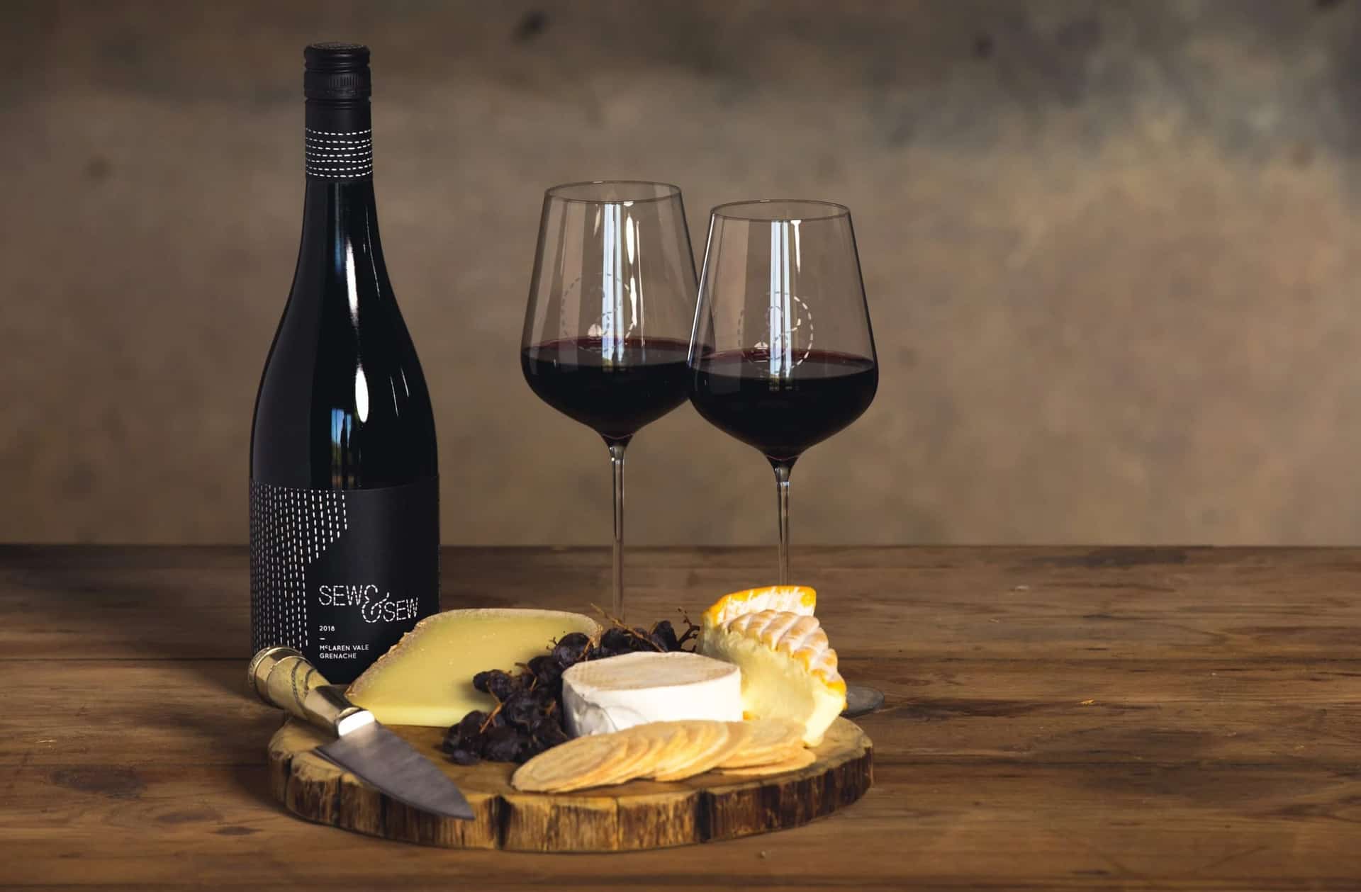 A bottle of Sew & Sew wine and two poured glasses on a timber table