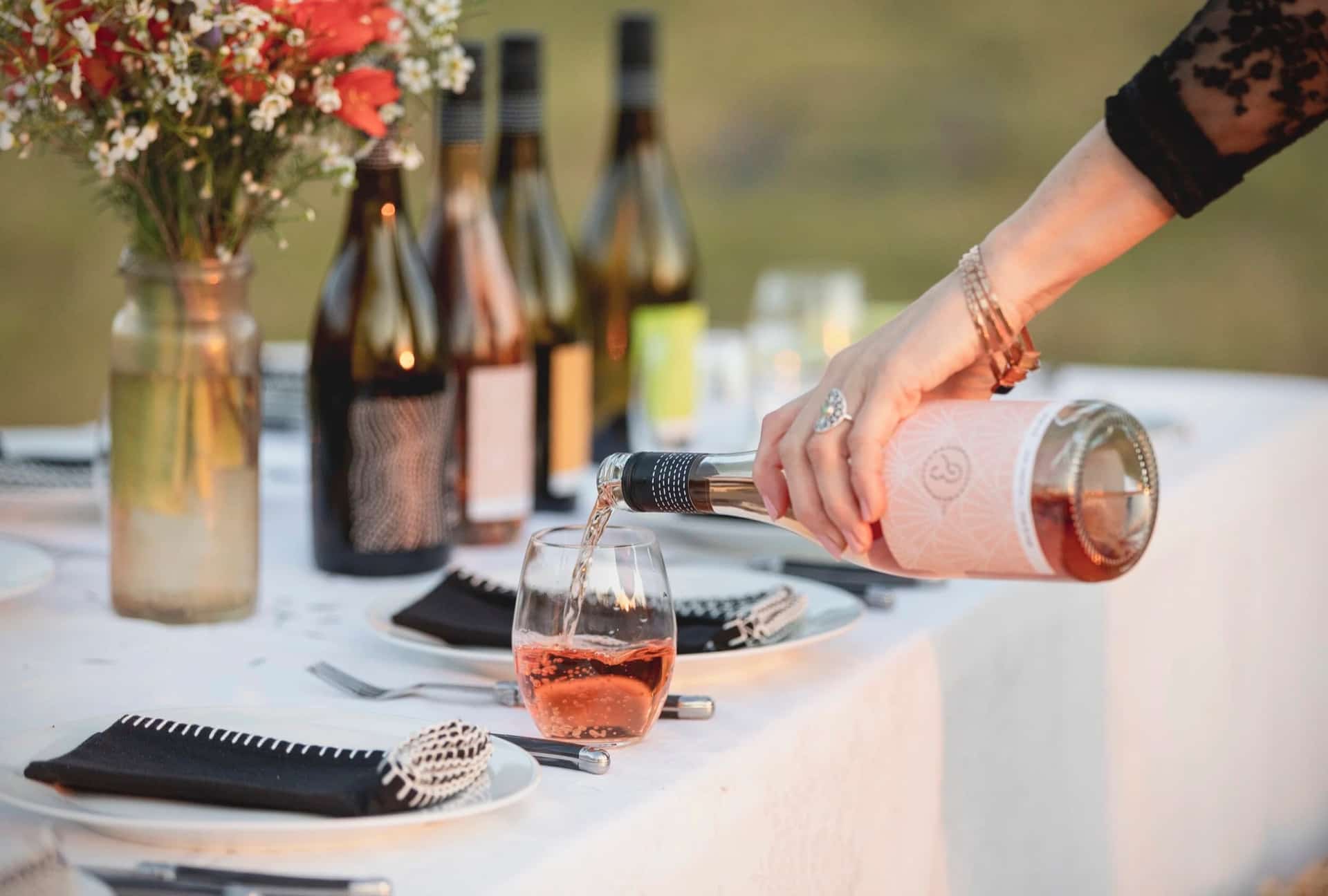 Sew & Sew rosé being poured into a glass at an outdoor table set with wildflowers and bottles from the range