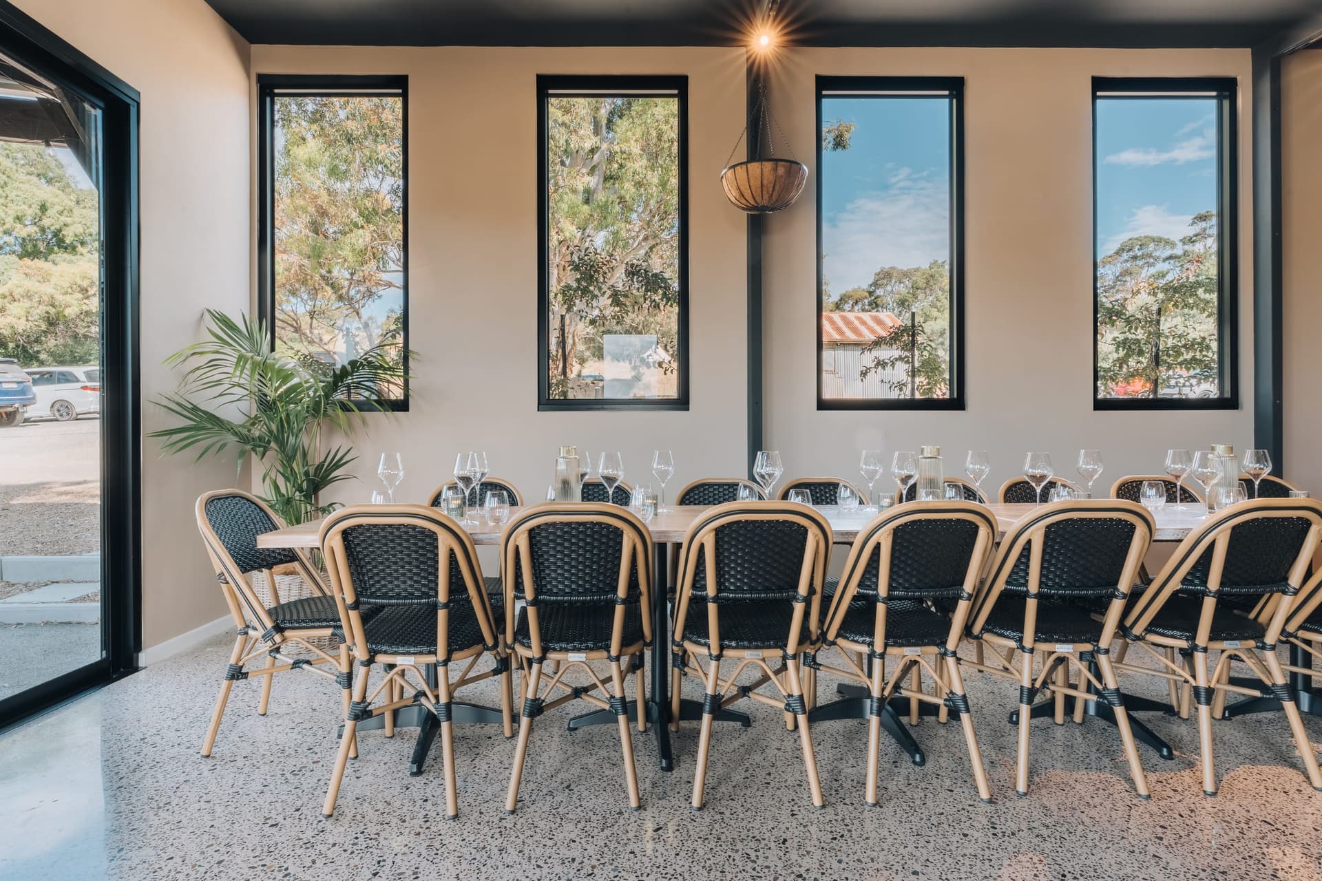 A long table set with wine glasses and rattan chairs beside the windows