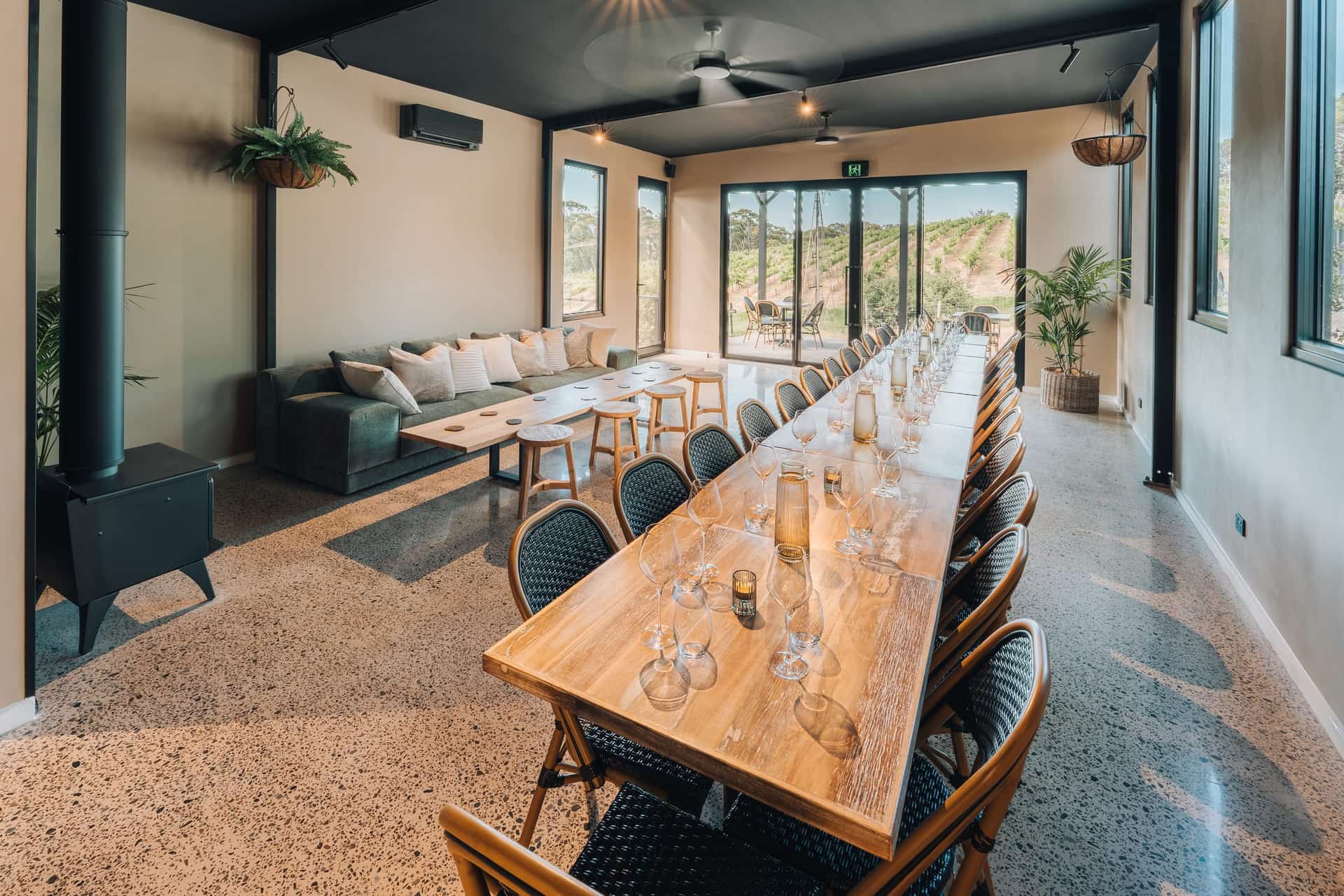 The Sew & Sew event space, a long table set with glasses beside the lounge, vineyard beyond the glass doors