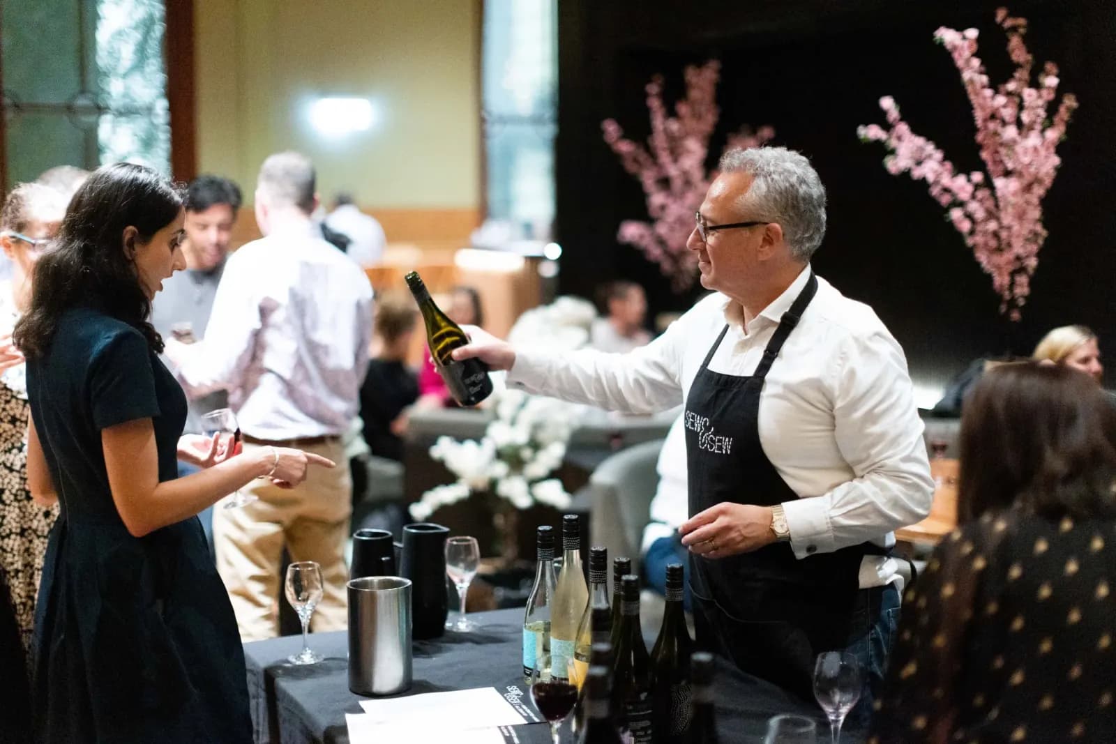 Pouring a Sew & Sew wine for a guest across the tasting table at Gather & Yarn