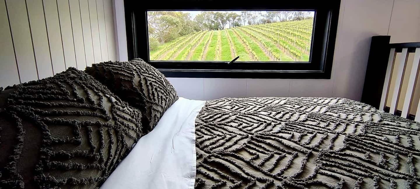 The loft queen bed in the tiny house, vineyard rows through the window