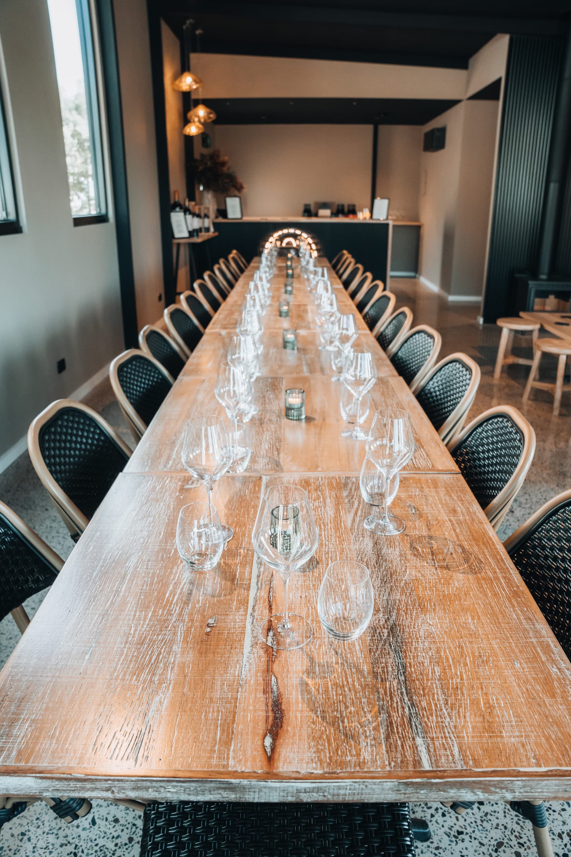 A long table dressed with glasses and rattan chairs, seen from above in the event space
